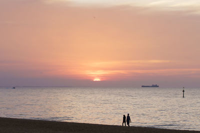 Silhouette people on beach against sky during sunset