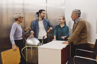 Multi-ethnic male and female business people with office equipment talking in elevator