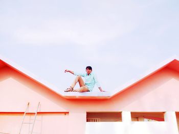 Low angle view of boy on building against sky