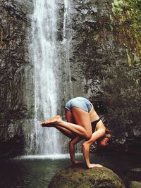 Woman doing handstand against waterfall