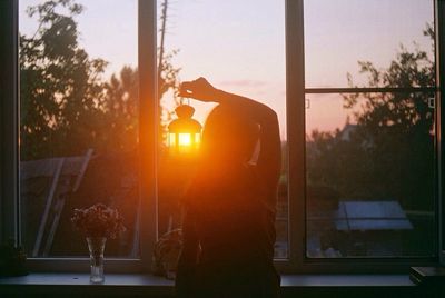 Silhouette of woman photographing against sky at sunset