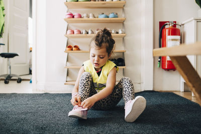 Girl sitting on carpet wearing shoes against rack in cloakroom at child care