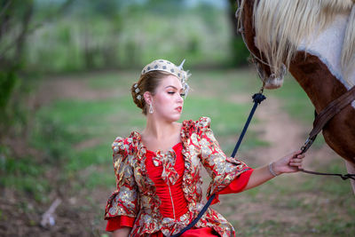 Woman in traditional clothing by horse against tree
