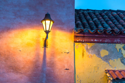 Illuminated lamp mounted on house wall at dusk