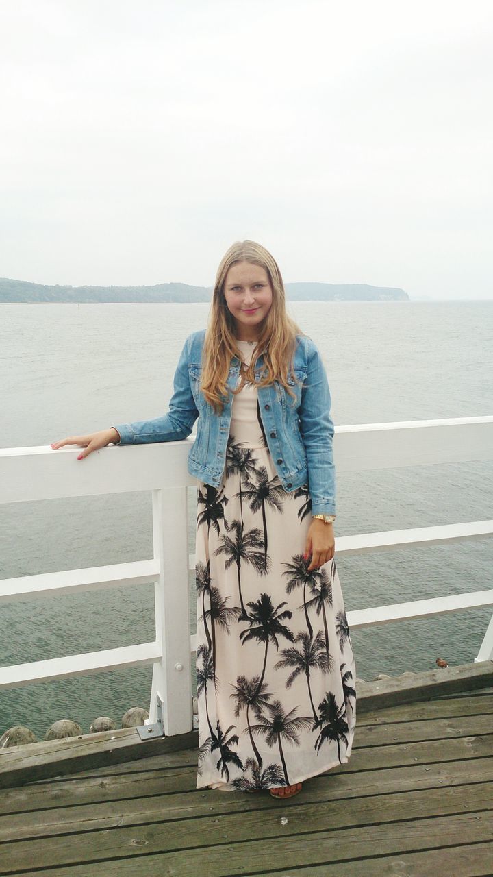 person, casual clothing, water, lifestyles, leisure activity, full length, standing, looking at camera, young adult, portrait, sea, railing, sitting, smiling, front view, clear sky, childhood, young women