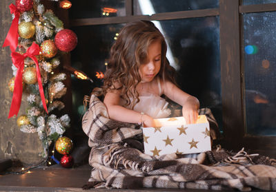 A little girl is looking at gift box and surprising near the window on christmas background.