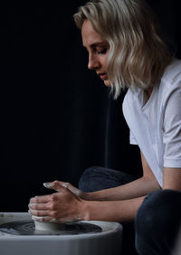 Side view of young woman using mobile phone against black background