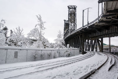 Snow covered railroad tracks by bridge