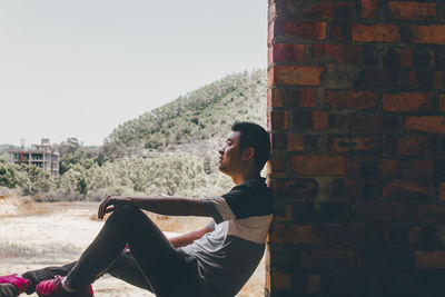 Side view of man sitting against wall