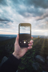 Midsection of person photographing smart phone against sky