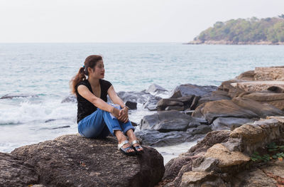 Full length of woman sitting on rock at beach