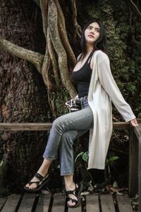 Young woman sitting on tree trunk against plants