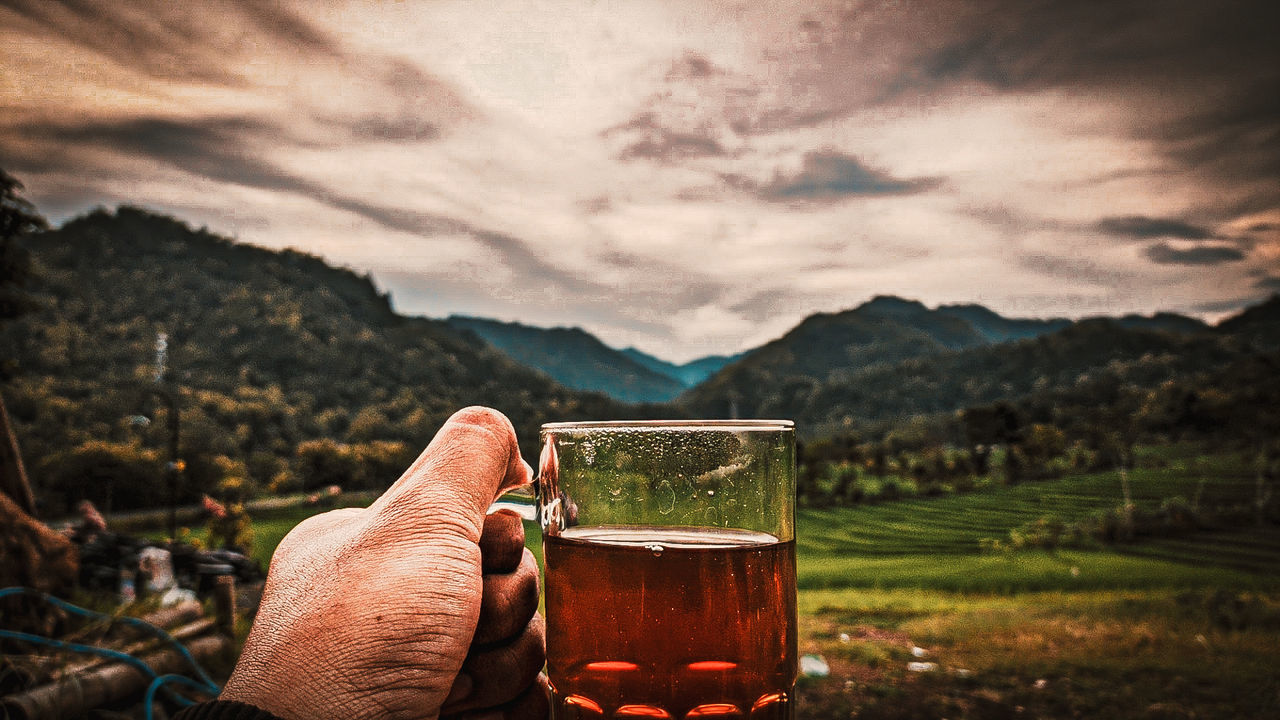 drink, refreshment, morning, food and drink, alcohol, mountain, sky, cloud, one person, beer, mountain range, nature, hand, glass, landscape, darkness, drinking glass, adult, leisure activity, sunlight, relaxation, household equipment, land, scenics - nature, personal perspective, environment, outdoors, holding, freshness, beauty in nature, plant, focus on foreground, reflection, lifestyles, rural scene, food, wine, tree