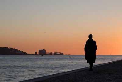 Silhouette man standing by sea against sky during sunset