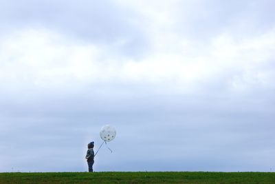 Man standing on grassy field against cloudy sky