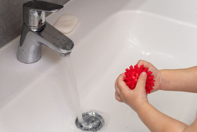 Cropped hands of child washing toy in sink