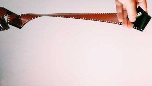 Cropped hand of person holding film reel against white background