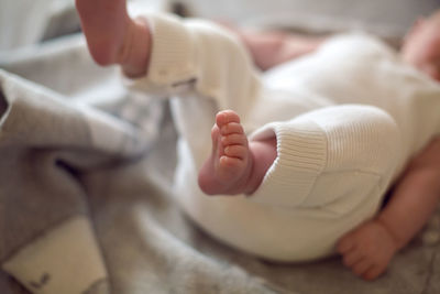 Close-up legs newborn baby is lying on a bed in a white knitted jumpsuit