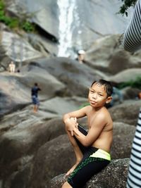 High angle view of shirtless boy sitting on rock