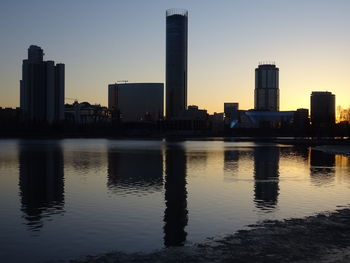 Silhouette buildings by river against sky during sunset
