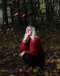 Portrait of beautiful young woman sitting on land in forest