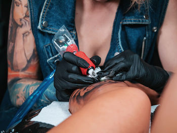 Midsection of tattooist making tattoo on customer