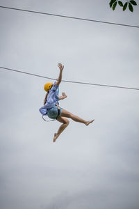 Low angle view of woman zip lining against sky