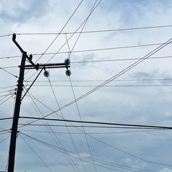Low angle view of electricity pylon against cloudy sky