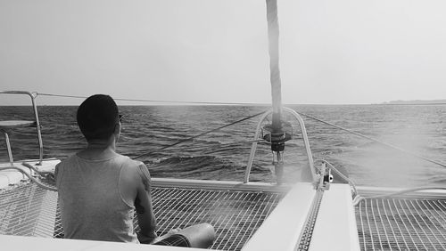 Rear view of man fishing in sea against clear sky