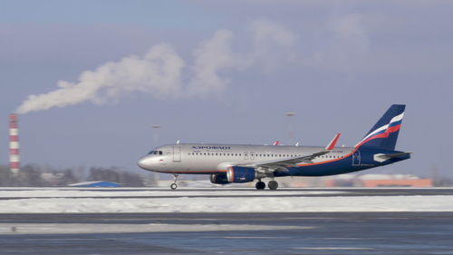 Airplane flying over airport runway against sky