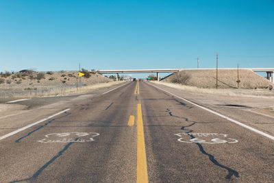 Empty country road passing through arid landscape against clear sky