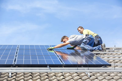 Low angle view of men working on roof against sky