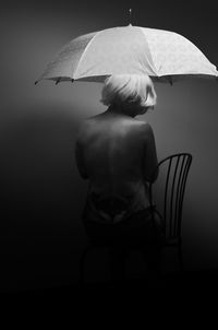 Rear view of sensuous woman with umbrella sitting on chair