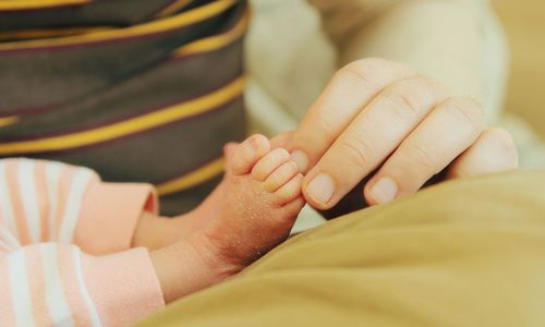 Cropped hand of mother holding newborn baby feet at home