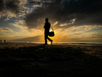 Silhouette man standing on beach against sky during sunset