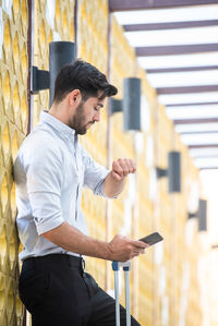 Side view of young man using mobile phone against building