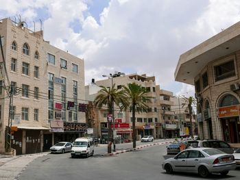 Cars on road by buildings in city against sky