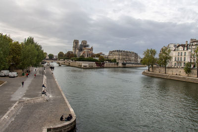 View of buildings by river against cloudy sky