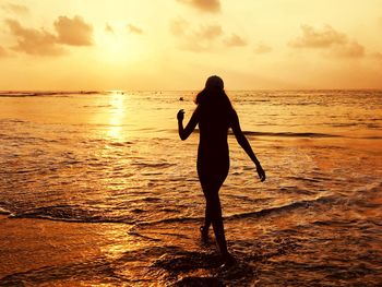 Silhouette woman walking on beach against sky during sunset