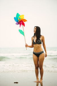 Full length of woman holding pinwheel toy while walking at beach