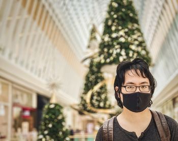 Portrait of young man standing against christmas tree and skylight inside mall.