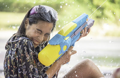 Side view of woman spraying water from gun while sitting outdoors