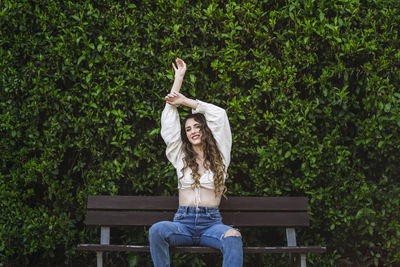 Woman sitting on bench against plants