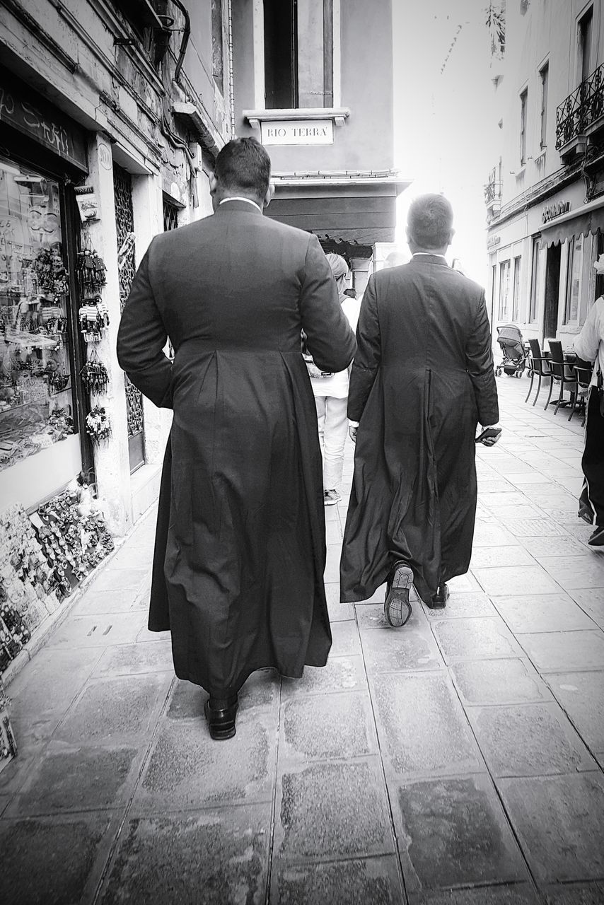 REAR VIEW OF PEOPLE WALKING ON STREET AMIDST BUILDINGS