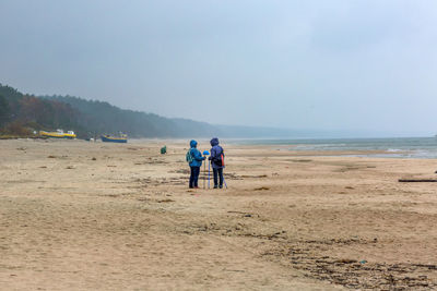 People with walking poles standing at sandy beach against sky