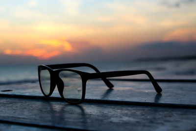 Close-up of silhouette eyeglasses on table against sea during sunset