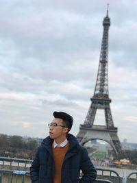 Young man standing against eiffel tower against sky