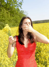 Woman in red dress standing amidst yellow flowers against sky