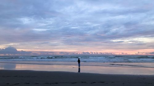 Man standing on beach against sky during sunset