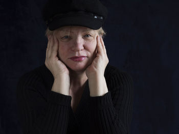 Portrait of senior woman wearing cap against black background